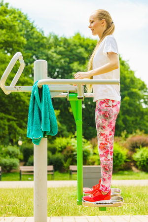 Young woman working out outside. Girl making exercises and training on public equipment in outdoor gym at park. Healthy lifestyle.の写真素材