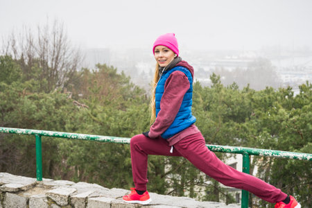 Outdoor sport exercises, sporty outfit ideas. Woman wearing warm sportswear training exercising, stretching legs outside during autumn.の写真素材