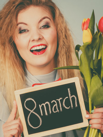 International women's day. Beautiful woman blonde hair fashion make up holding red yellow tulips and frame board with message 8 March. Toned imageの写真素材