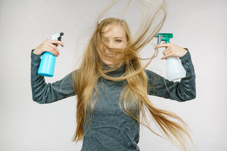 Young female messy long blonde hair holding bottle, applying hair spray.の写真素材