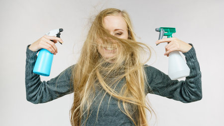 Young female messy long blonde hair holding bottle, applying hair spray.の写真素材