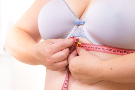 Close up of plus size woman wearing bra with measure tape measuring her chest under breast. Bra fitting and underwear concept.の写真素材