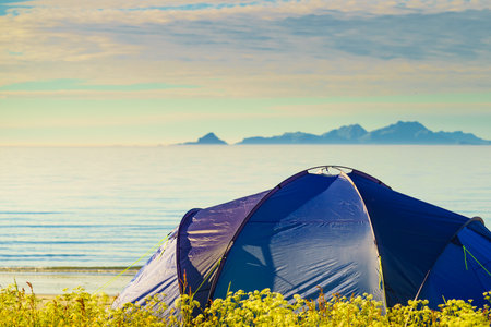 Blue tent on Gimsoysand beach in summer. Mountains on sea horizon. Camping on ocean shore. Lofoten archipelago Norway. Holidays and adventure.の写真素材
