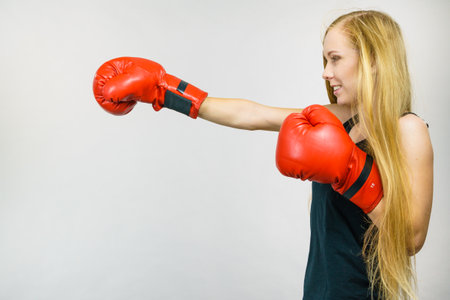 Blonde long hair woman in big red boxing gloves. Female fight for equal rights for women. Side view. Gender equality concept.の写真素材
