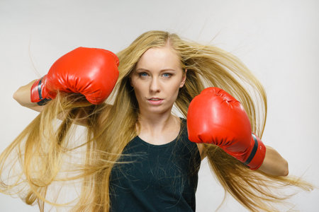 Blonde long hair young woman in big red gloves boxing, playing sports. Female fight for equal rights for women.の写真素材