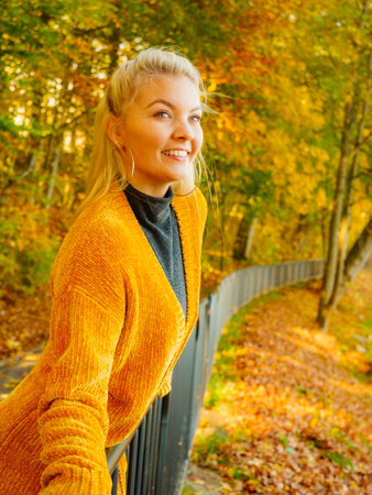 Young woman wearing fashionable outfit yellow cardigan walking in autumnal park in sunny day.の写真素材