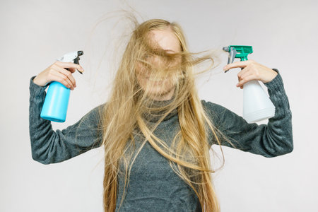 Young female messy long blonde hair holding bottle, applying hair spray. Haircare.の写真素材