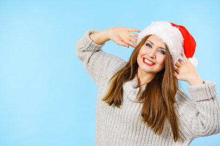 Young brunette woman in christmas santa hat smiling, on blueの写真素材