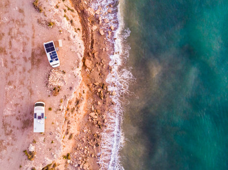 Aerial view. Two camper vehicles with solar photovoltaic panels on roof camping on sea, coastal cliff in Spain. Caravan vacation.の写真素材