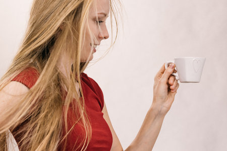 Blonde girl with blowing long hair holds heart shaped coffee cupの写真素材