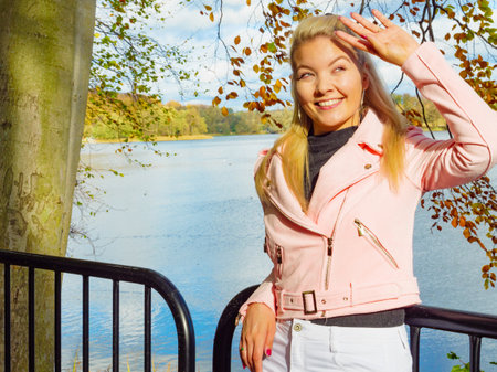 Blonde young woman wearing fashionable outfit. Happy female in pink leather jacket walking relaxing in autumn park.の写真素材