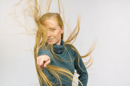 Smiling girl with blowing long blonde hair pointing with finger at you.の写真素材