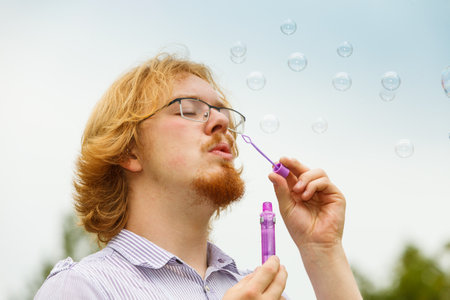 Happiness and carefree concept. Young man having fun blowing soap bubbles on natureの写真素材
