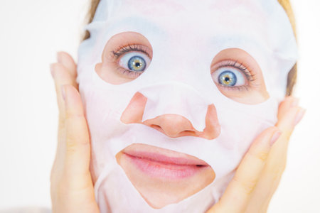 Woman applying sheet mask on her face. Girl taking care of skin complexion. Beauty treatment. Skincare.の写真素材