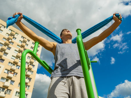 Handsome guy relaxing after outdoor workout. Fit man feeling healthy, enjoying sun. Exercising on public gym equipment in the open air.の写真素材