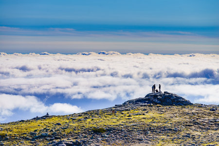 Hikers in silhouette stands on rock in mountains above clouds. Torre mountain peak, Serra da Estrela, the highest place in Continental Portugal.の写真素材
