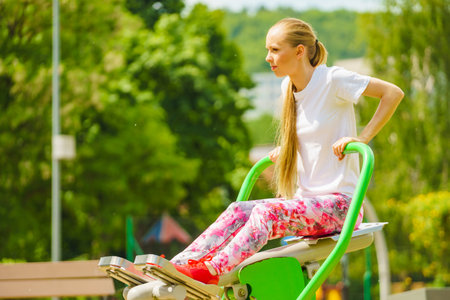 Young woman working out in the outdoor gym. Girl making exercises and training at public sport area in city park. Healthy lifestyle.の写真素材