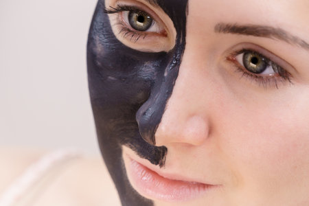 skincare. Woman with charcoal facial mask, deep cleanser on half face. Beauty, spa and acne treatment.の写真素材