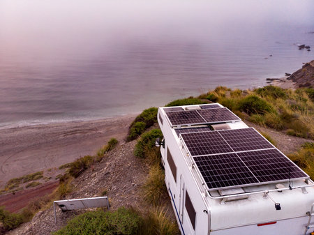 Aerial view. Camper rv with solar photovoltaic panels on roof camping on cliff sea shore in wintertime, foggy misty morning. Mediterranean region of Villaricos, Costa Almeria in Andalusia, Spainの写真素材