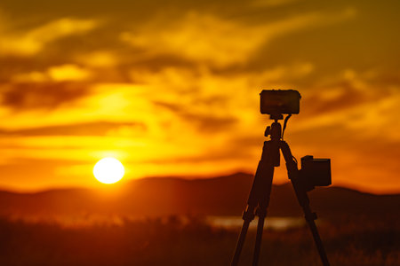 Professional camera on tripod taking picture of sunset.の写真素材