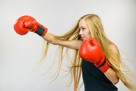 Blonde long hair woman in big red boxing gloves. Female fight for equal rights for women. Side view. Gender equality concept.の写真素材