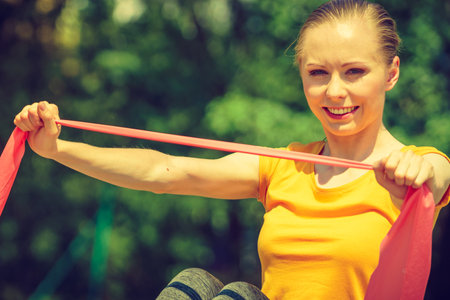 Young woman exercises outdoor in park, using gym accessory, resistance band, strap elastic. Staying fit and healthy.の写真素材