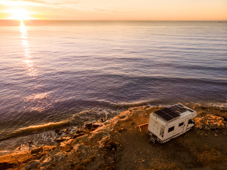 Caravan with solar panels on roof camping on coastal cliff at sunrise. Mediterranean sea in Spain.の写真素材