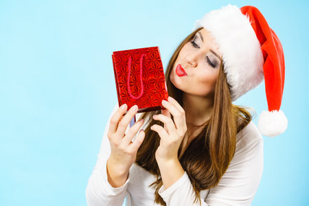 Woman is happy to give Christmas gifts. Female wearing santa claus hat holding present red gift bag, on blueの写真素材