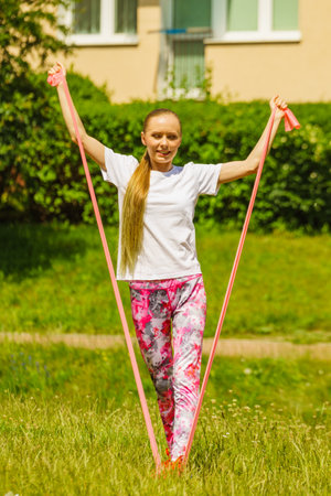 Young woman exercises outdoor in park, using gym accessory, resistance band. Staying fit and healthy.の写真素材