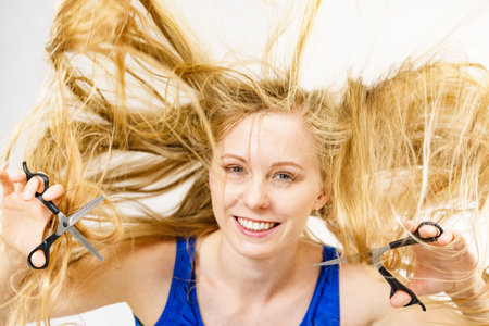Haircut coiffure haircare concept. Girl with blowing long blond hair holding scissors, showing work tools, normal and thinning shears.の写真素材