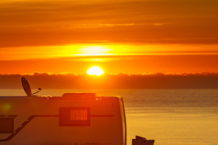 Sun rising over sea horizon and camper rv camping on beach seashore. Holidays in Spain, travel with motor home.の写真素材