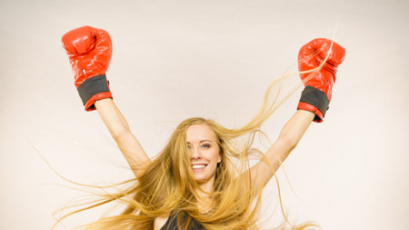 Blonde long hair woman wearing big red gloves standing with arms up, celebrating success. Female...