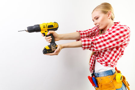 Young determined woman using drill doing home renovation. Female construction worker having driller tool drilling wall.の写真素材