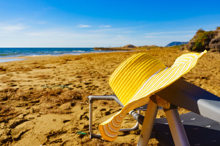 Summer and holidays, resting on seaside. Chair and yellow straw hat on sandy beach sea shore.の写真素材