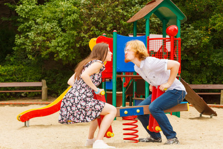 Happy couple having fun together outdoor. Happiness, great relationship. Man and woman fooling around, ride on swing at playground.の写真素材
