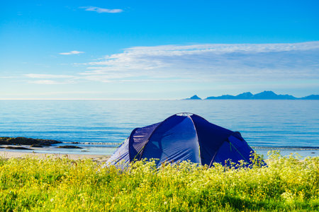 Blue tent on Gimsoysand beach in summer. Mountains on sea horizon. Camping on ocean shore. Lofoten archipelago Norway. Holidays and adventure.の写真素材