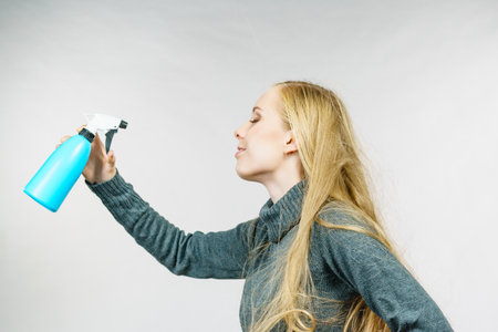 Young female long blonde hair holding bottle, applying spray water treatment on face or hair. Side viewの写真素材