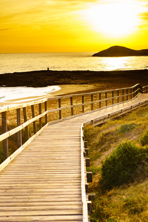 Sunset over beach seashore with wooden path to sea water. Cala Magre in Calblanque Regional Park, Murcia region Spain.の写真素材