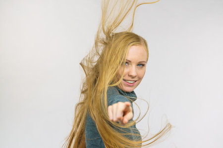 Smiling girl with blowing long blonde hair pointing with finger at you.の写真素材