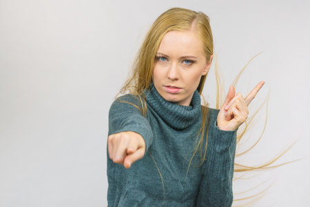 Young woman pointing at you and weighing her finger. Rejecting gesture, disagree sign. Serious face expression.の写真素材