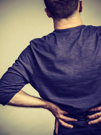 View from back on man having terrible loins pain ache. Guy suffering from health problem.