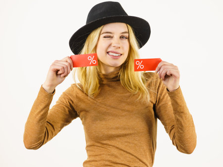 Woman in hat showing tag with shopping sale percentage sign enjoying cheap clothing. Female wearing stylish outfit.の写真素材
