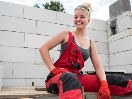 Smiling woman wearing workwear working on construction site. Partially built new home early stage.の写真素材