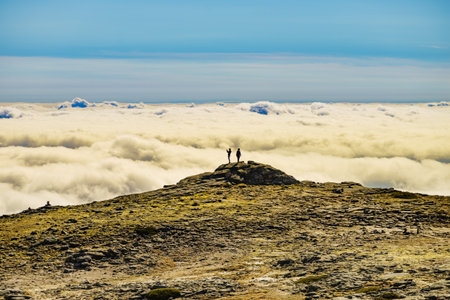 Hikers in silhouette stands on rock in mountains above clouds. Torre mountain peak, Serra da Estrela, the highest place in Continental Portugal.の写真素材
