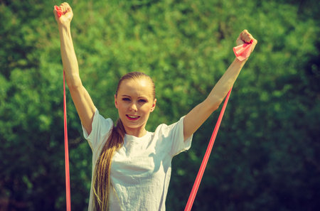 Woman doing exercise outdoor in park, using gym accessory, resistance band. Staying fit and healthy.