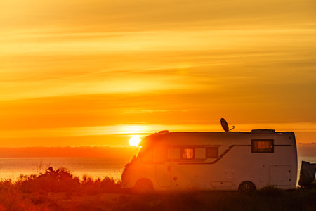 Sun rising over sea horizon and camper rv camping on beach seashore. Travel with motor home.の写真素材