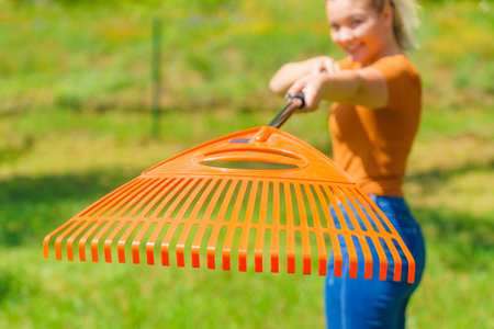 Woman working on her backyard, using gardening tools, standing with orange rake.の写真素材