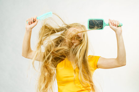 Girl with blowing long blonde hair holding brush and comb. Haircut, haircare concept.