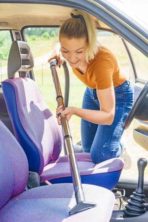 Female hoovering seat of car. Auto interior cleaning with vacuum cleaner.の写真素材