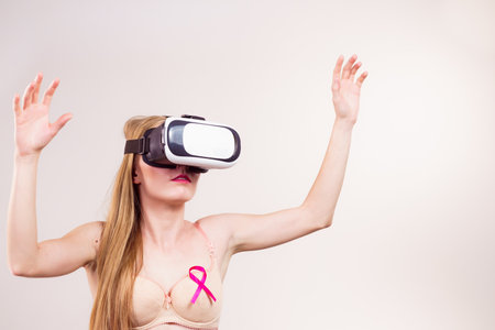 Woman wearing bra with pink ribbon and virtual reality goggles headset, vr box. Treatment and prevention of breast cancer.の写真素材